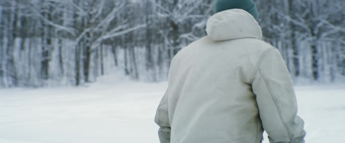 Man walking in the snow towards horses in the forest