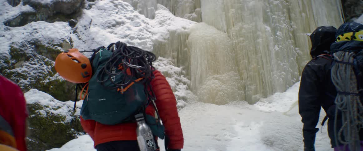 Three people with climbing gear walk over to a ice covered mountain