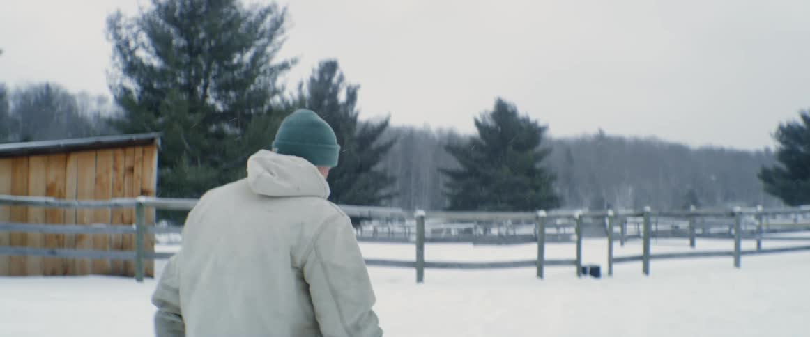 A man walks across a snowy pasture on a farm