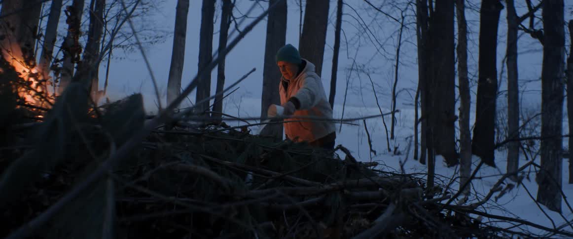 A man throws a liquid from a cup that makes an outdoor stick fire larger