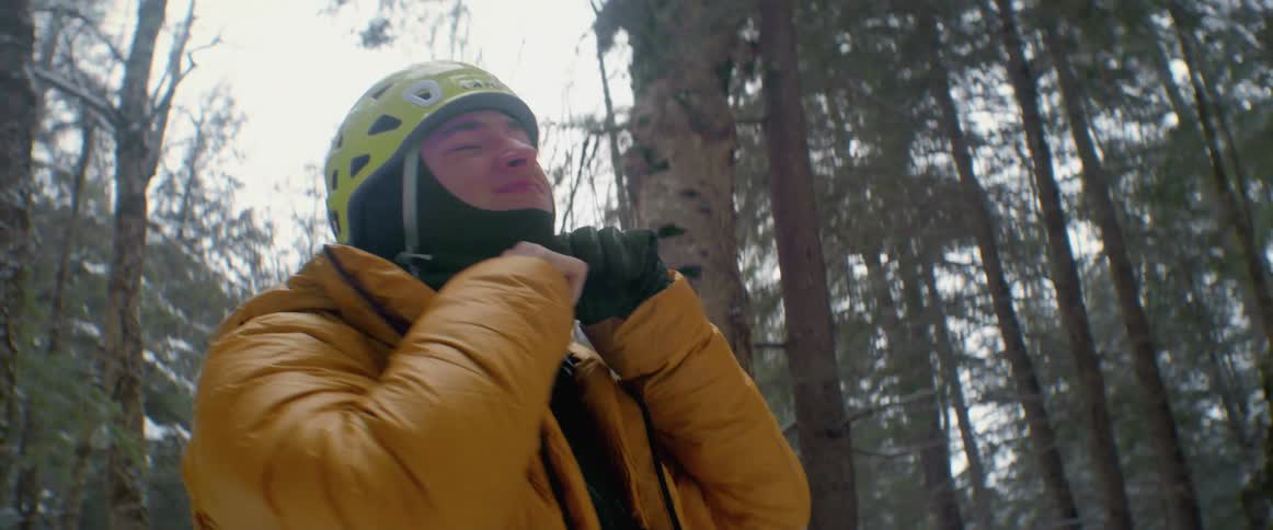 A man straps on a helmet while standing in the forest