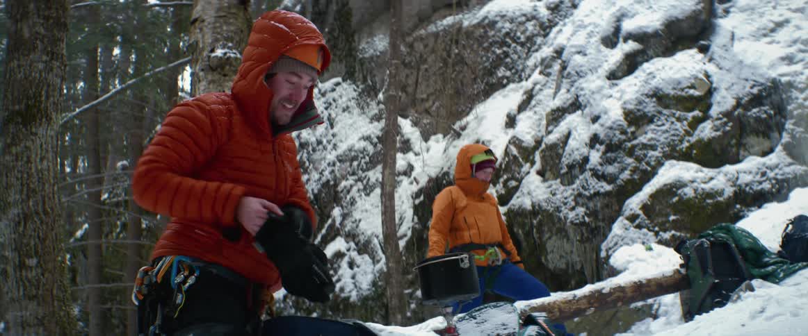 Man puts pot to heat as he and another stand on snow covered mountain