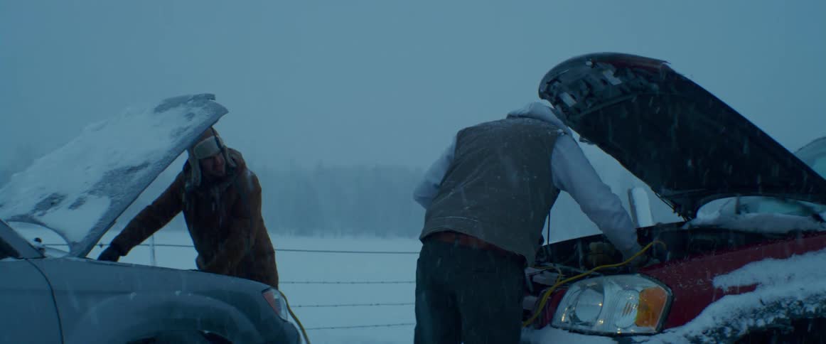 Two men try to jump a vehicle battery standing outside in a snow storm