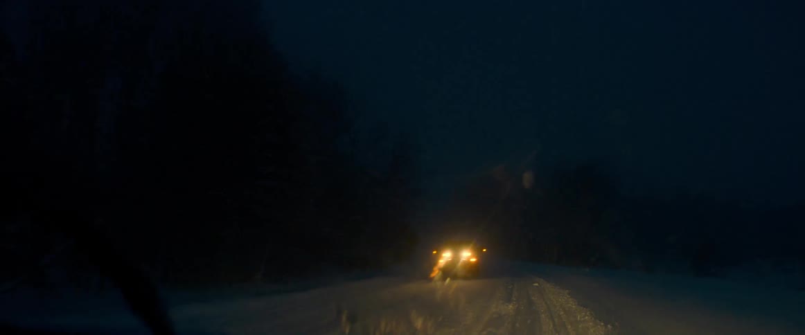Traveling on a snow covered road at night and the headlights from an oncoming vehicle shine in the windshield