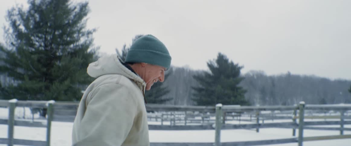 A man walking through the snow past empty livestock pens