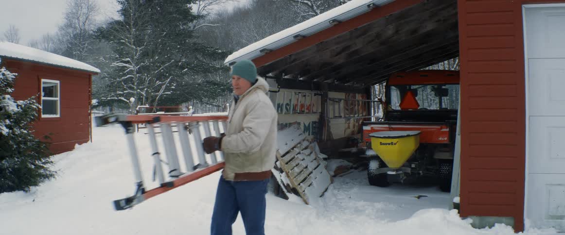 A man carries a ladder out of a storage shed next to his garage on a ranch
