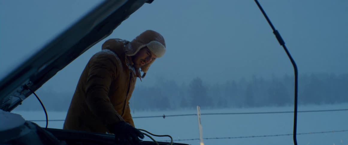 A man checks the engine compartment of his vehicle during a snow storm