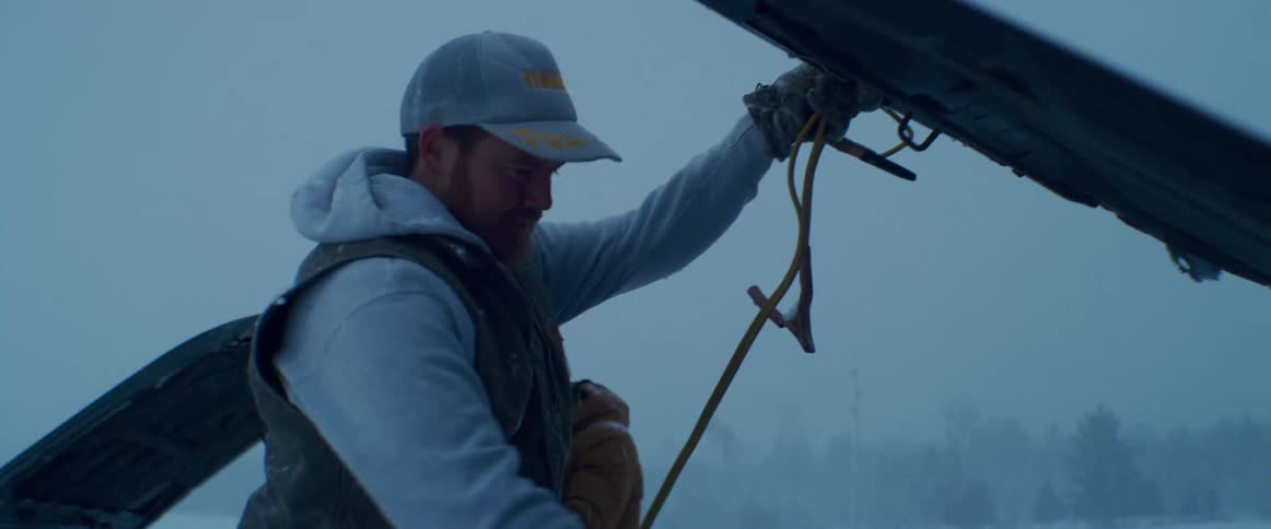 A man lifts the hood of a vehicle outside in a snow storm
