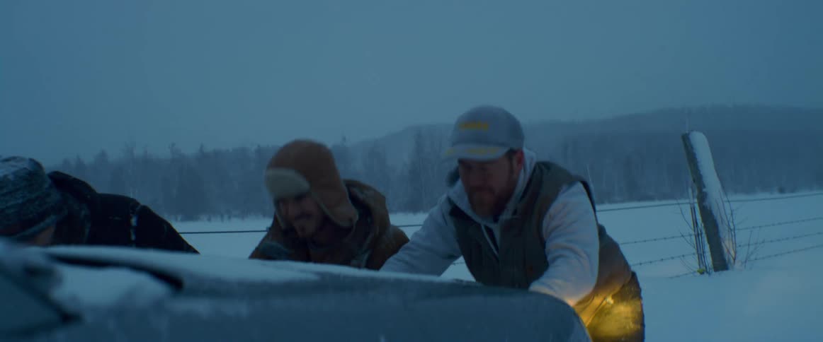 Three men push a vehicle on a snow covered road