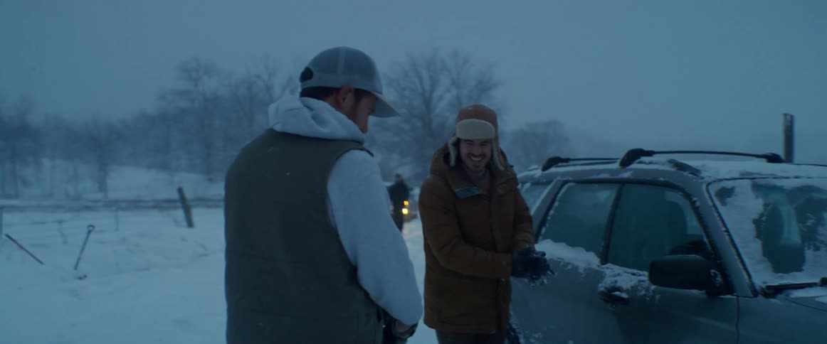A man walking over to help out a man whose car is stuck in the snow