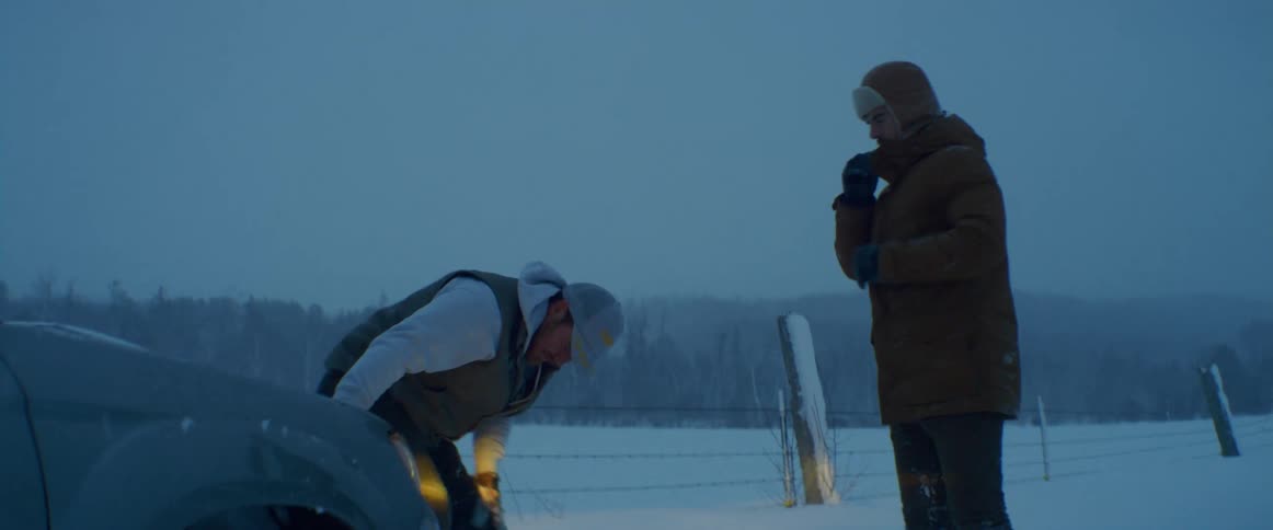 Men take a look at a car stuck in the snow discussing what to do