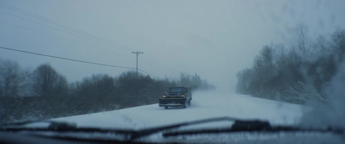 Traveling on a snow covered forest road during a blizzard and a truck with a snow plow passes by