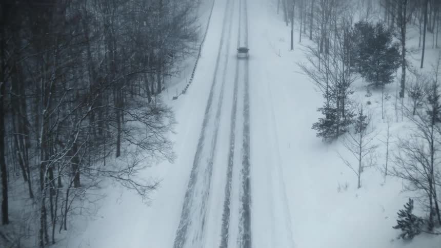 Aerial view of a truck traveling on a snow covered forest road during a blizzard