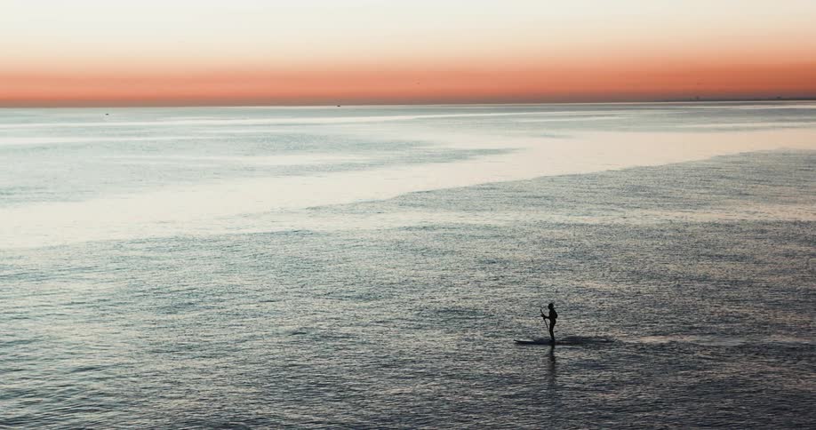 Aerial of person paddle boarding in the ocean at sunrise