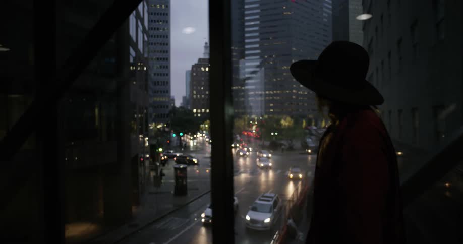 A woman in a hat walks through a glass bridge over a busy street
