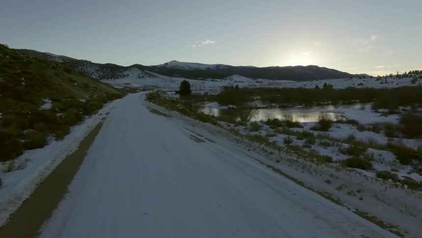 A snow covered road next to a body of water and hills