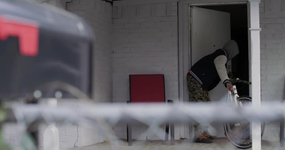 A man takes his bike out of a building and lifts it up