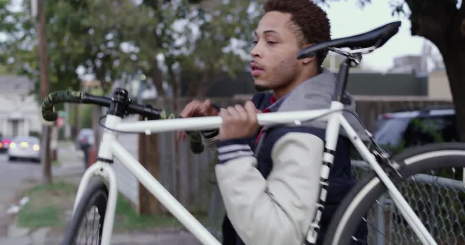 A man wearing a jacket carries his bike through a gate