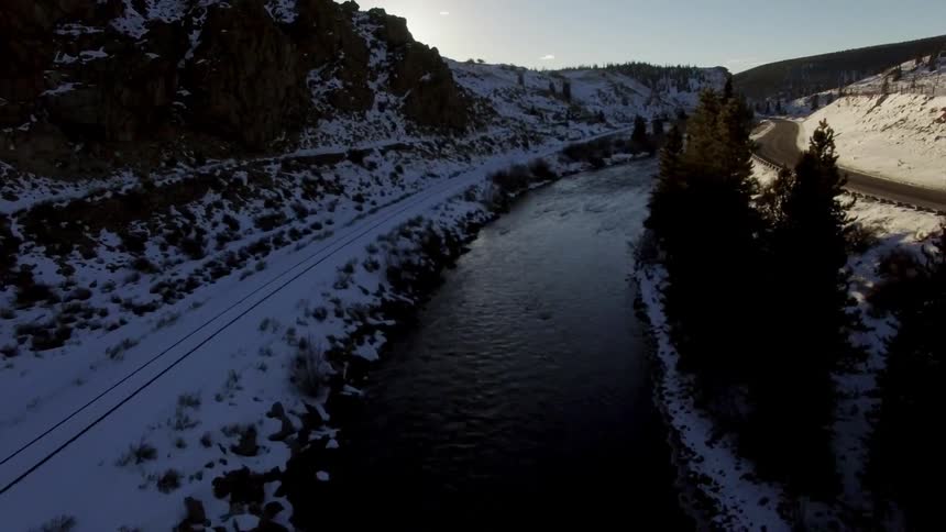 A river flowing between a road and snow-covered cliffs