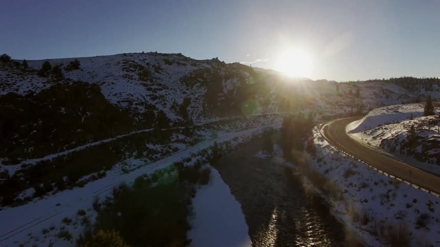 Aerial view moving over a snow-covered landscape with a river and bright sun