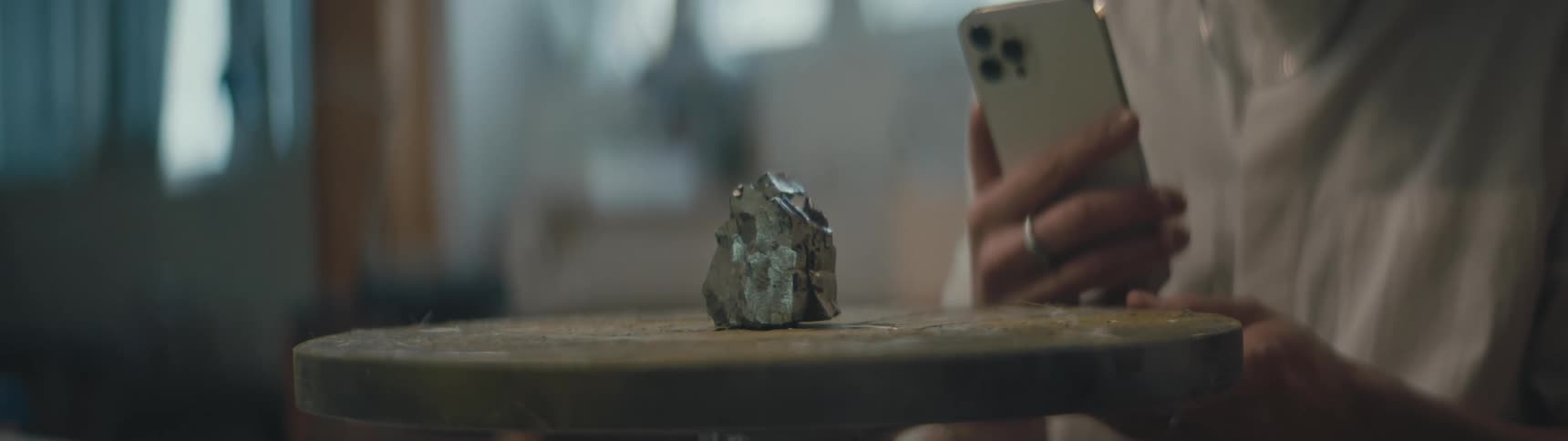 A woman is kneeling in a living room and filming a large mineral on a table during the daytime