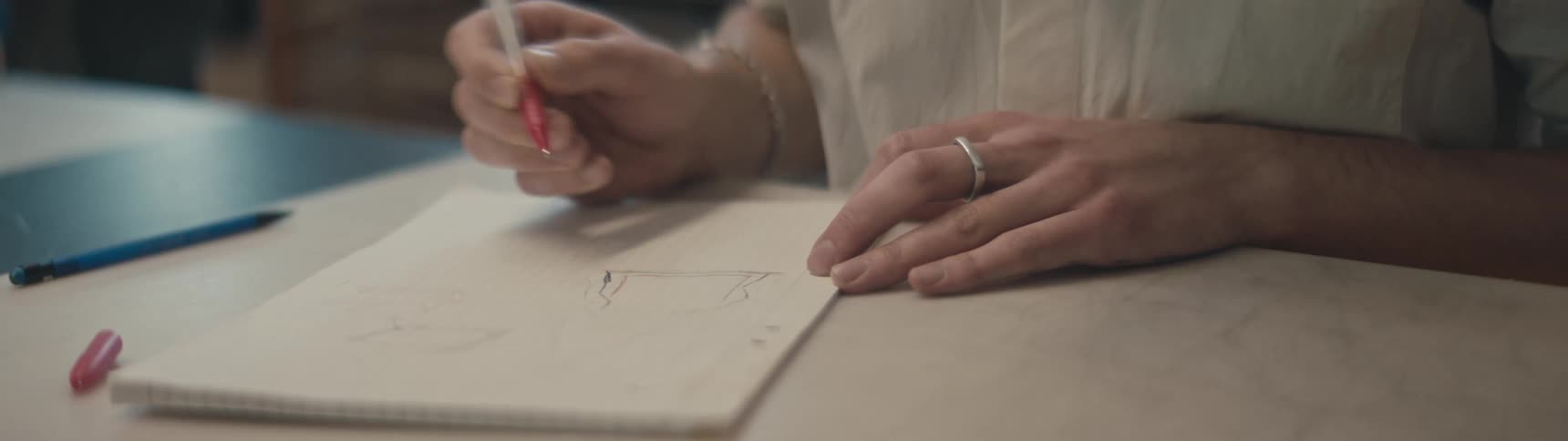 Woman with white shirt and rings makes drawing in notebook