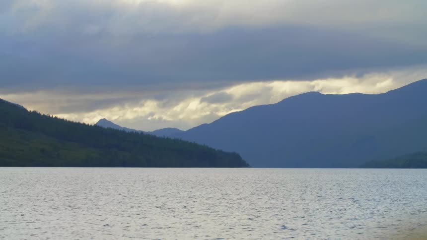 The water ripples as it moves and there are mountains in the distance under a cloudy sky