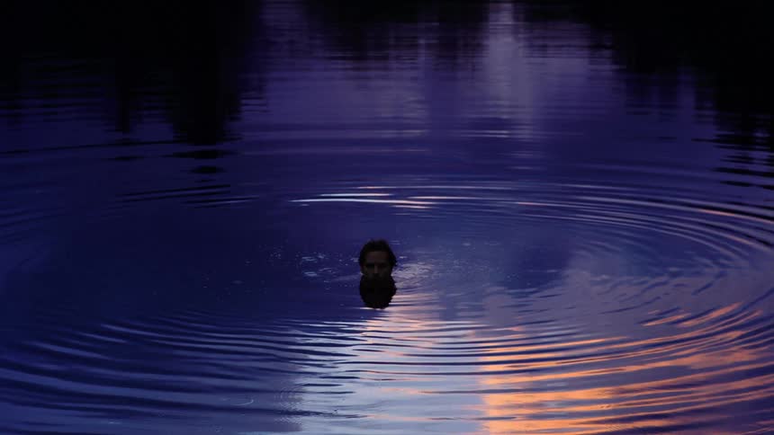 A man stands in a lake with just his head peeking out from under the water