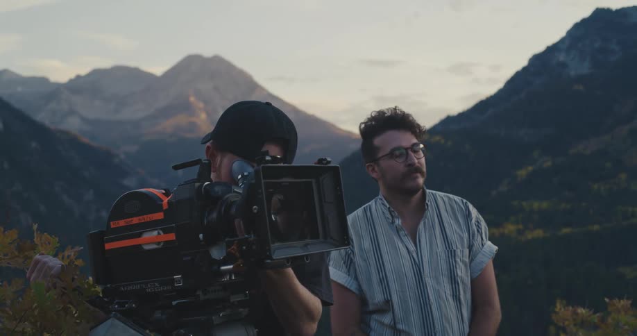 A man looks through his friends camera as they film in the mountains