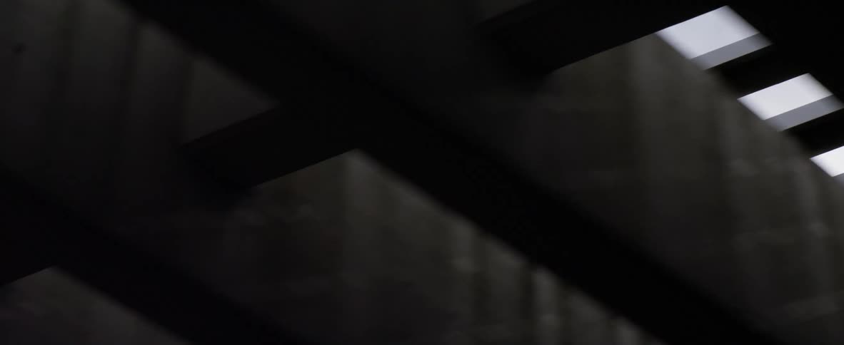 Cross beams sit through and over large parallel concrete sections showing glimpses of the sky