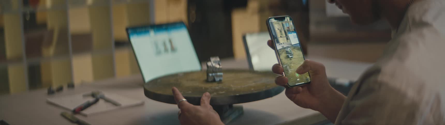 A piece of iron pyrite is on a round turning table and someone is taking a picture of it with their cell phone