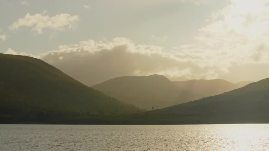 The water ripples as it moves and there are mountains in the distance under a cloudy sky