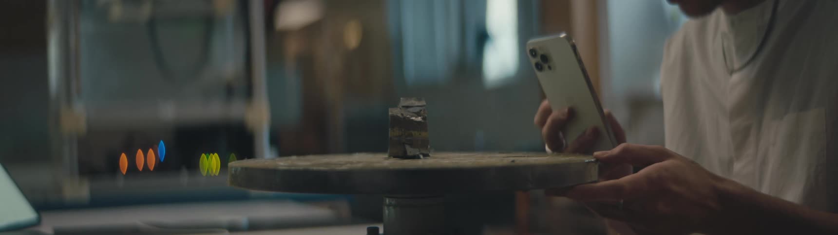 A piece of iron pyrite is on a round turning table and someone is taking a picture of it with their cell phone