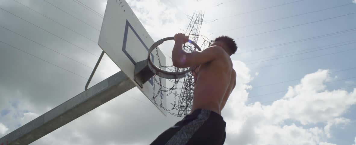 Man does pull ups using metal basketball hoop under a electric transformer tower as a storm cloud flows across the sun
