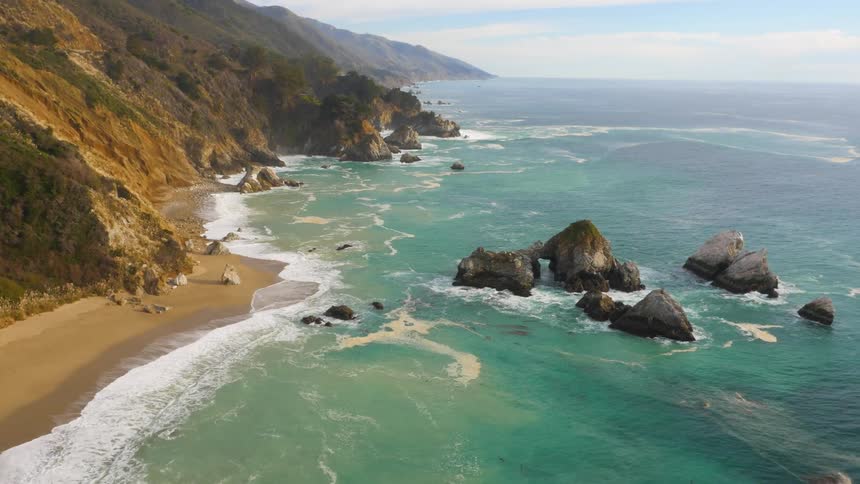 Aerial view of the coastline as waves splash against the rocks and roll in over the beach