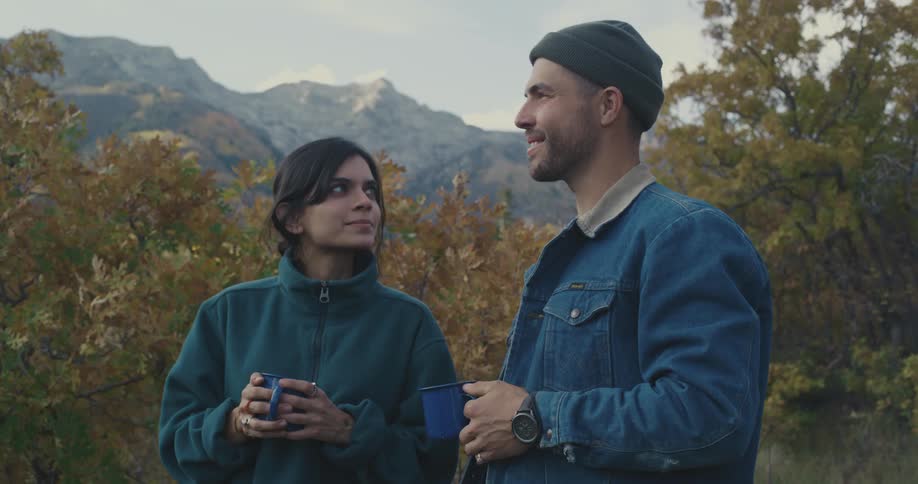 A couple holding coffee mugs standing in the forest talking