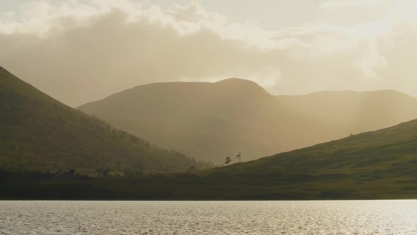 The water ripples as it moves and there are mountains in the distance under a cloudy sky
