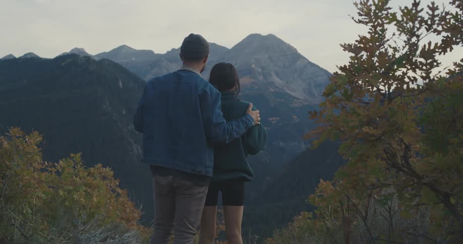A man and woman embrace standing on a mountain top