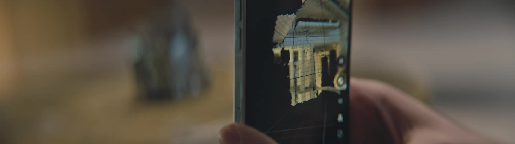 Hands hold and turn a phone as it films and renders a 3d image of a metal object and room