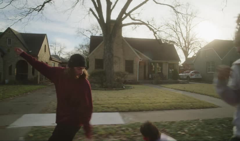A group of friends laugh as they skateboard through a neighborhood and one falls down