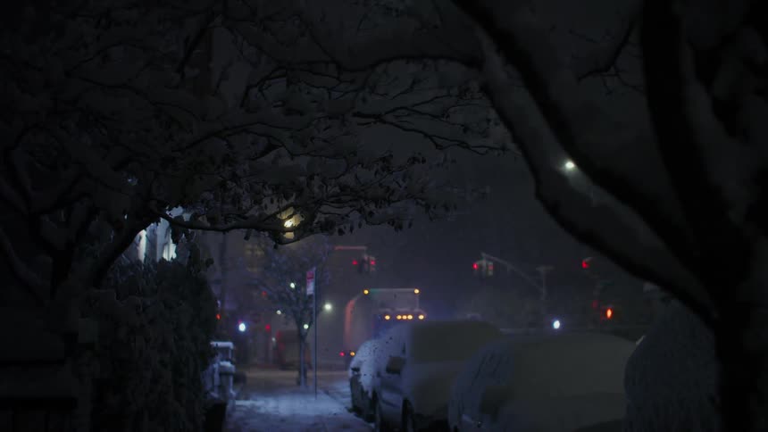 A large truck stops at a red light on a quiet street during a snow storm