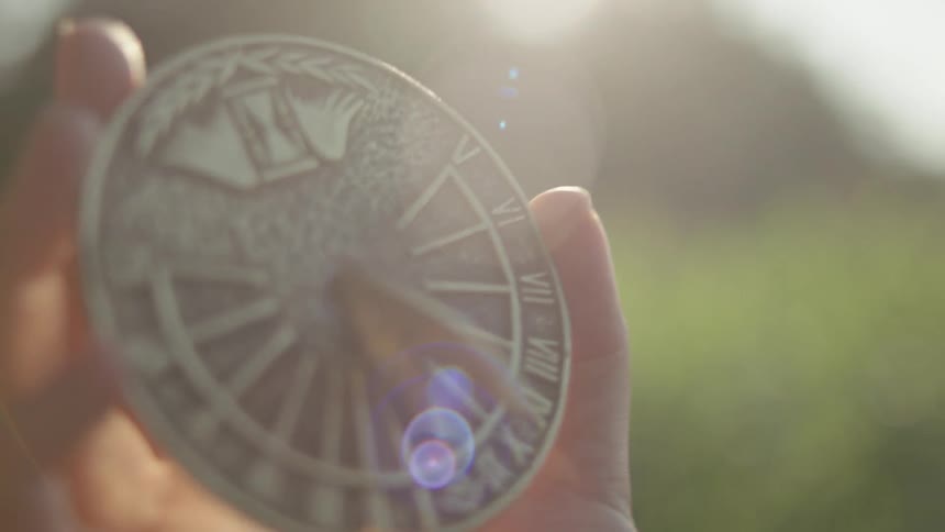 The sun shines brightly on a girls hand holding a sundial