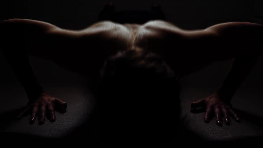 Shirtless white man doing push ups alone at a dark empty room