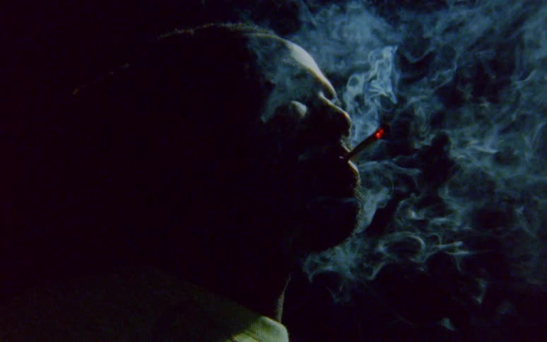 A black man is smoking in the darkness