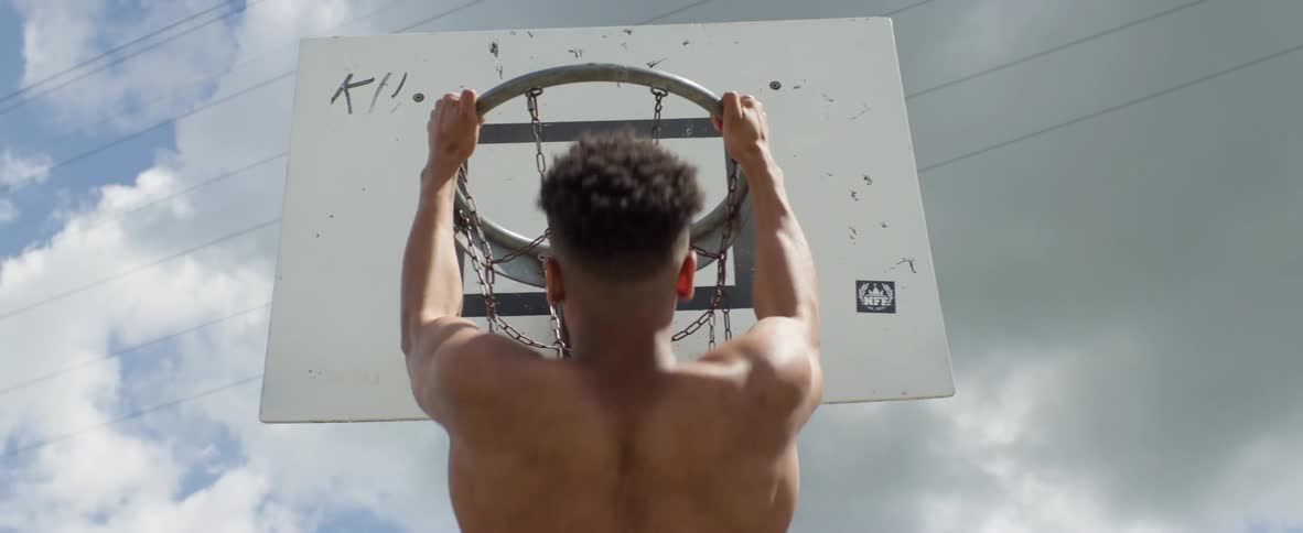 A man uses a basketball hoop to do pull ups at an apartment complex