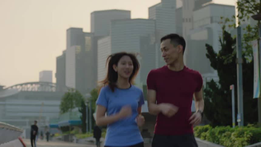 Asian man and asian woman jogging while talking and laughing together at a public space in a big city with multiple skyscraper at the background