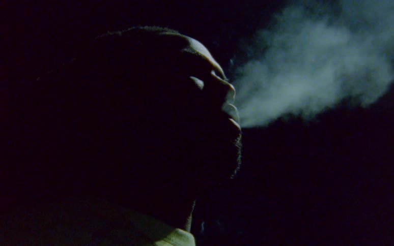 Man with dreadlocks and beard smokes a cigarette in the dark