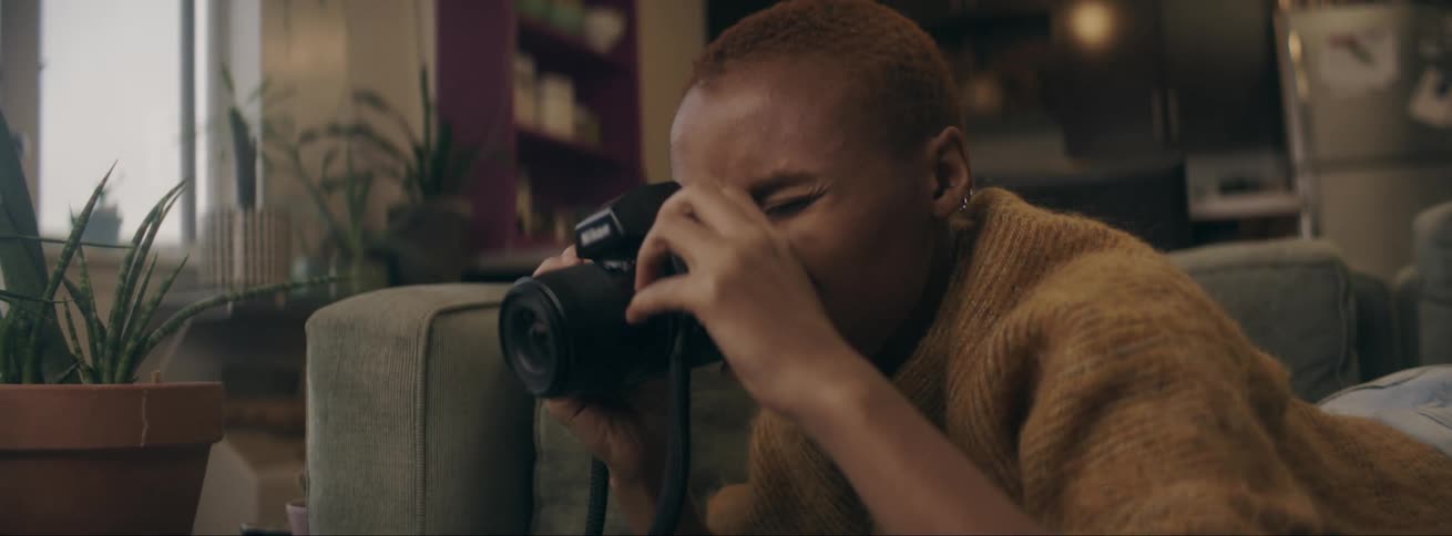 A woman lies on the couch and looks through the lens of her dslr camera