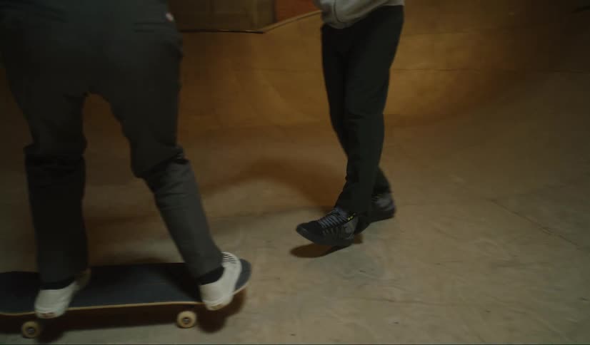 A man holds a womans hands as she tries to skateboard in an enclosed skate park area