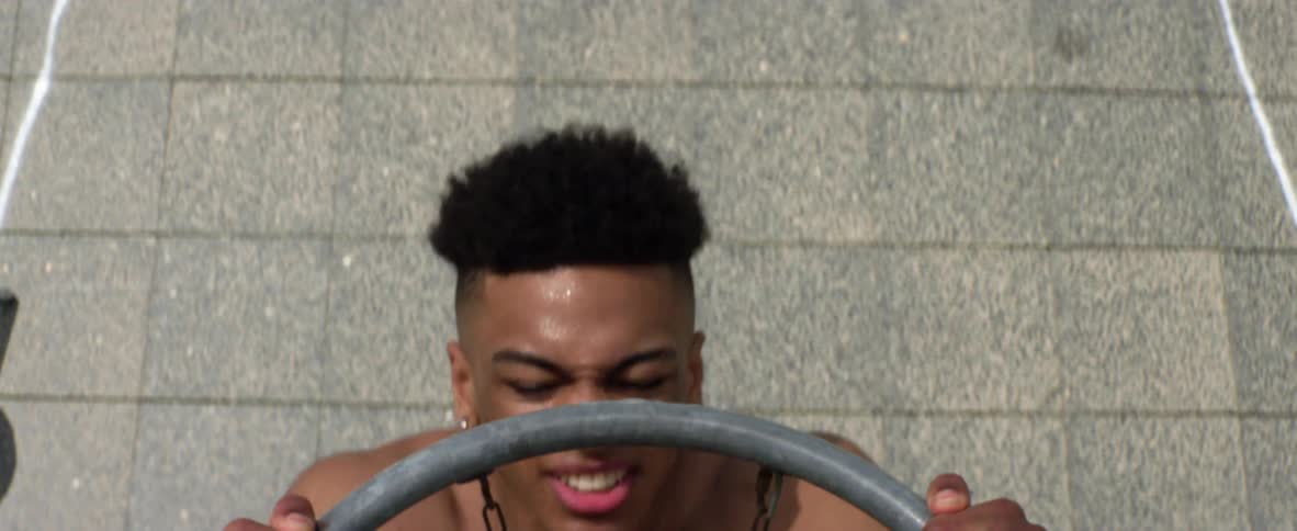 Shirtless young black man doing pull ups at a basketball hoop